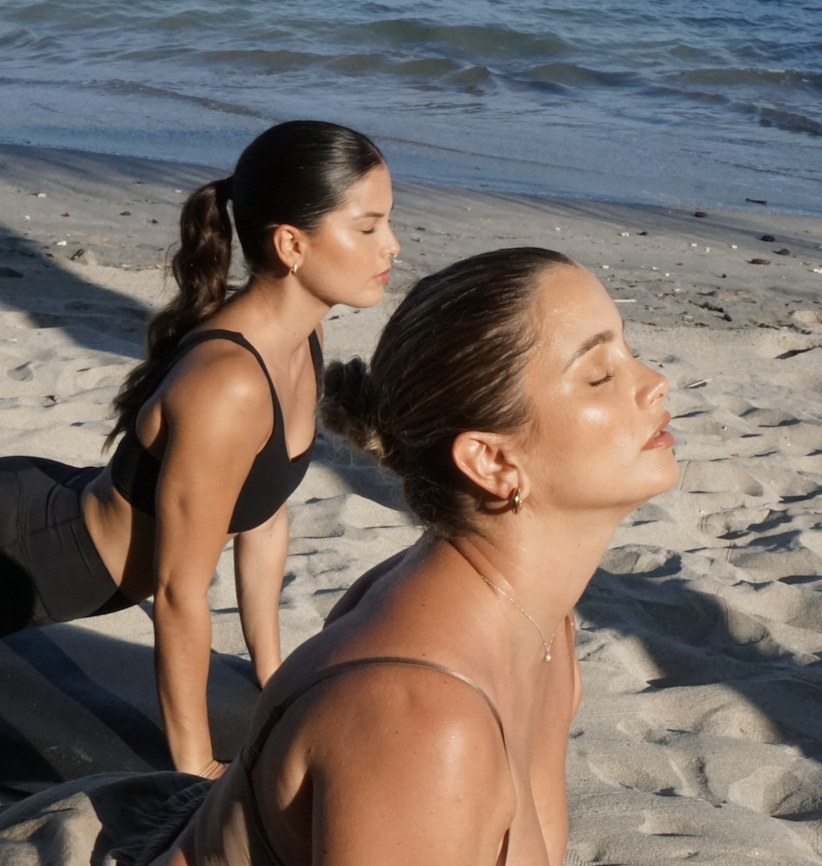 Dos mujeres practicando yoga sobre sus mats frente al mar